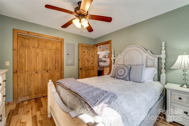 bedroom with electric panel, ceiling fan, light wood-type flooring, and a closet