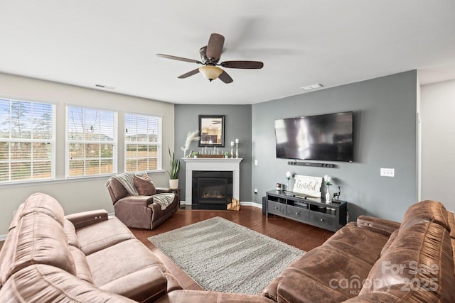 living room with a glass covered fireplace, visible vents, wood finished floors, and ceiling fan