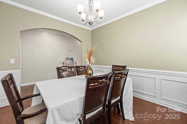 dining room with a decorative wall, a wainscoted wall, ornamental molding, a notable chandelier, and dark wood-style flooring