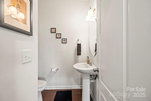 half bathroom with toilet, wood finished floors, and baseboards