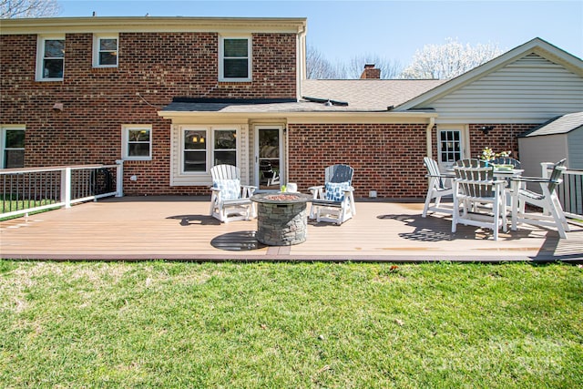 back of house with an outdoor fire pit, a yard, a wooden deck, brick siding, and a chimney