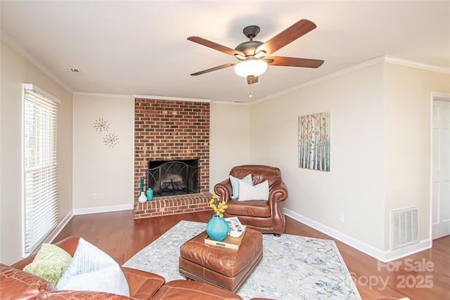 living room with wood finished floors, visible vents, baseboards, crown molding, and a brick fireplace