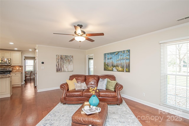 living room with crown molding, wood finished floors, visible vents, and baseboards