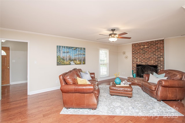 living area with wood finished floors, baseboards, ceiling fan, crown molding, and a brick fireplace