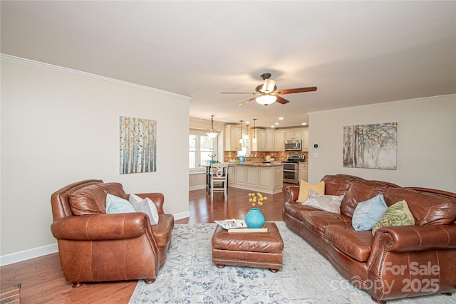 living room with crown molding, light wood-style flooring, a ceiling fan, and baseboards