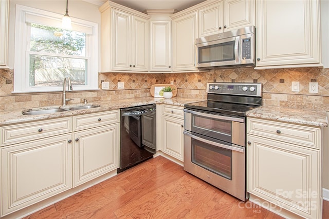 kitchen featuring cream cabinetry, light wood-style flooring, a sink, appliances with stainless steel finishes, and decorative backsplash