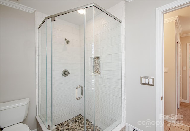 bathroom featuring toilet, a shower stall, and crown molding