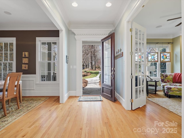 entryway with a wainscoted wall, wood finished floors, plenty of natural light, and ornamental molding