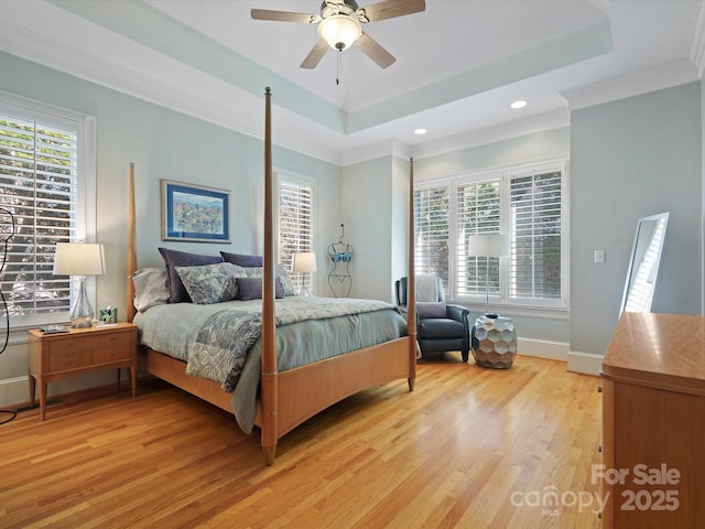 bedroom featuring light wood-type flooring, ornamental molding, baseboards, a raised ceiling, and ceiling fan