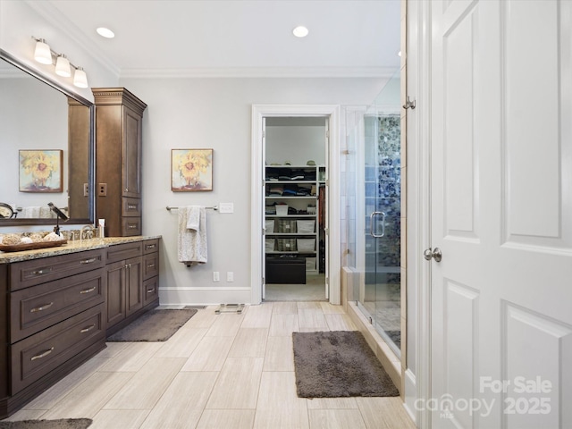 bathroom featuring vanity, baseboards, a shower stall, a walk in closet, and crown molding