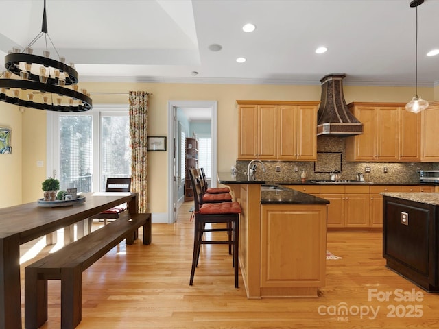 kitchen with light brown cabinetry, light wood-type flooring, an inviting chandelier, and a sink