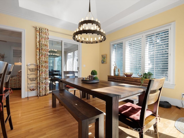 dining room featuring crown molding, baseboards, a chandelier, a tray ceiling, and light wood-style flooring