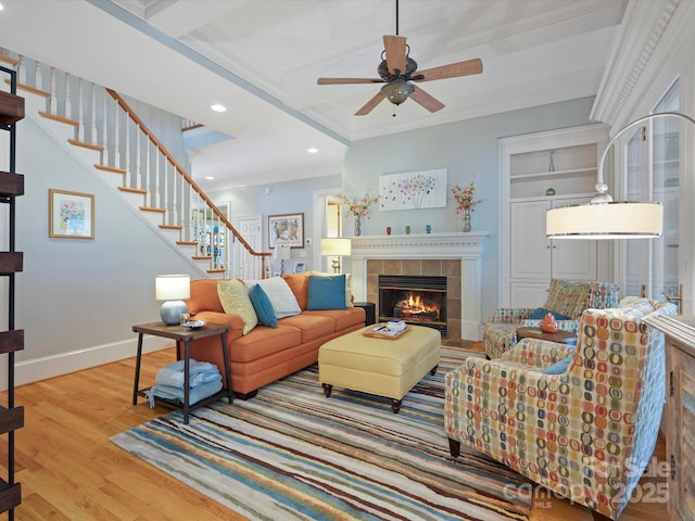 living area featuring stairway, wood finished floors, baseboards, a ceiling fan, and a tiled fireplace