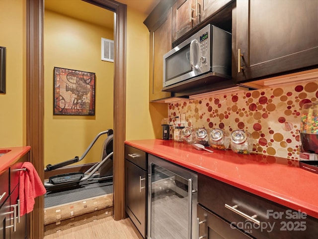 kitchen with beverage cooler, visible vents, decorative backsplash, dark brown cabinets, and stainless steel microwave