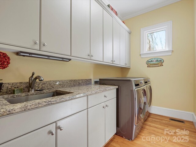 laundry area with visible vents, crown molding, washing machine and dryer, cabinet space, and a sink