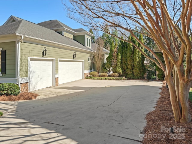 view of side of home with concrete driveway, an attached garage, and a shingled roof