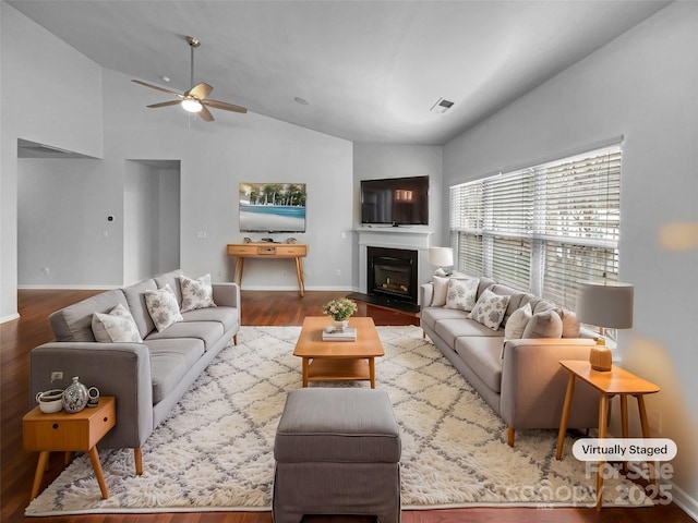 living area featuring wood finished floors, visible vents, baseboards, a fireplace with flush hearth, and vaulted ceiling