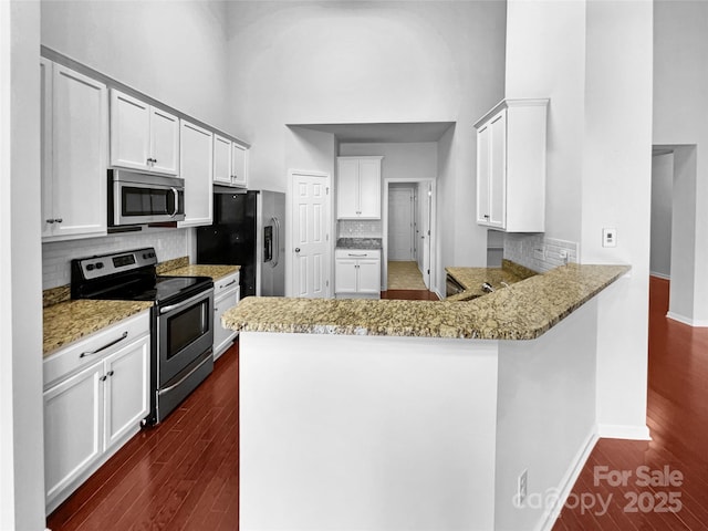 kitchen featuring a peninsula, stainless steel appliances, dark wood-type flooring, and a high ceiling