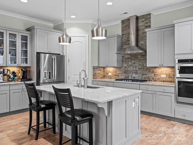 kitchen with a sink, a kitchen breakfast bar, backsplash, appliances with stainless steel finishes, and wall chimney exhaust hood