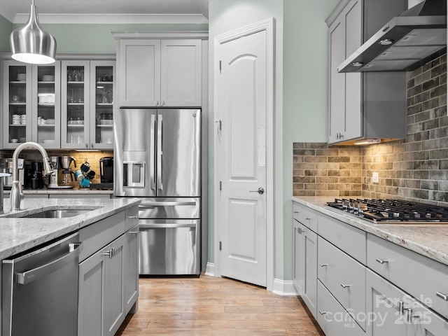 kitchen featuring light wood-type flooring, ornamental molding, appliances with stainless steel finishes, wall chimney exhaust hood, and a sink