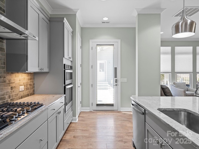 kitchen featuring appliances with stainless steel finishes, gray cabinetry, wall chimney range hood, and ornamental molding