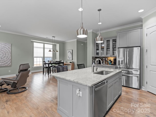 kitchen featuring light wood finished floors, gray cabinetry, a center island with sink, stainless steel appliances, and a sink