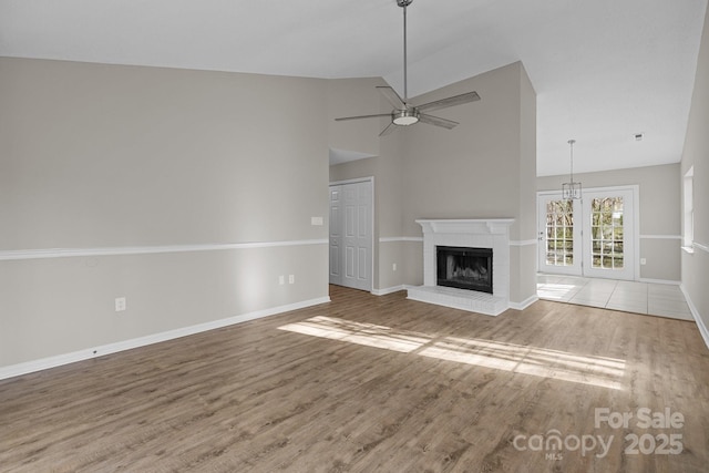 unfurnished living room with high vaulted ceiling, a ceiling fan, wood finished floors, baseboards, and a brick fireplace