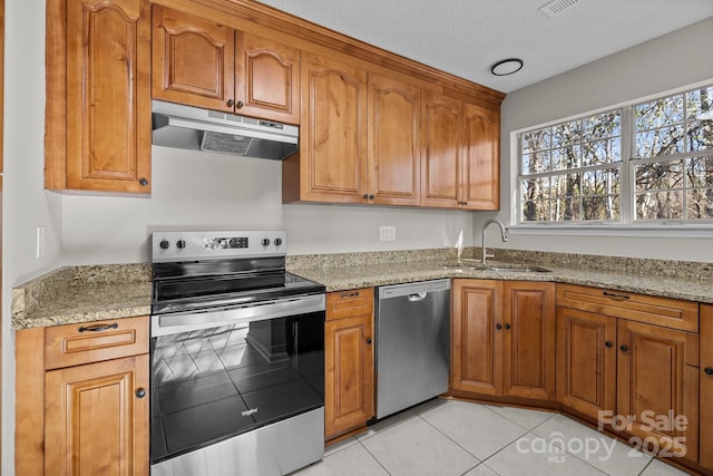 kitchen featuring under cabinet range hood, light tile patterned floors, light stone counters, stainless steel appliances, and a sink