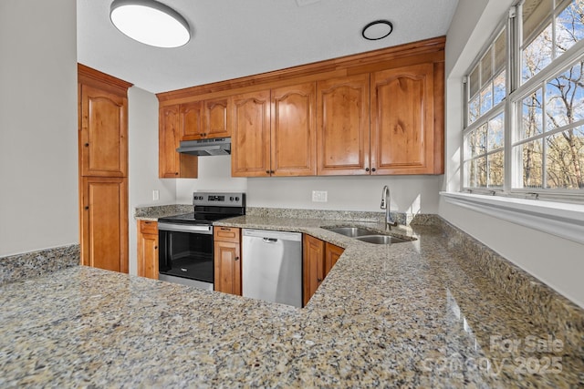 kitchen with under cabinet range hood, light stone counters, a sink, stainless steel appliances, and brown cabinetry