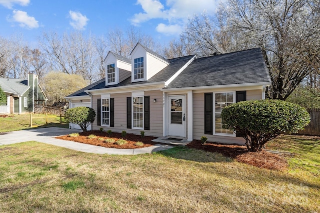 new england style home with concrete driveway, roof with shingles, a front yard, and fence