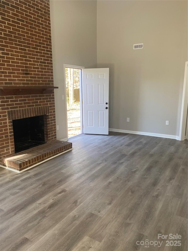 unfurnished living room with visible vents, baseboards, a fireplace, a towering ceiling, and wood finished floors