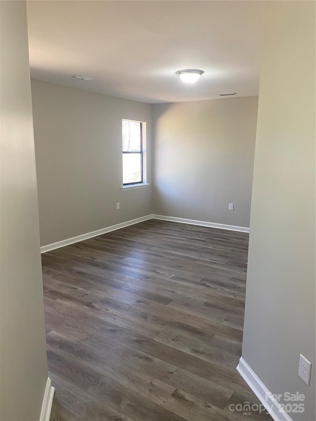 spare room featuring visible vents, baseboards, and dark wood-style floors