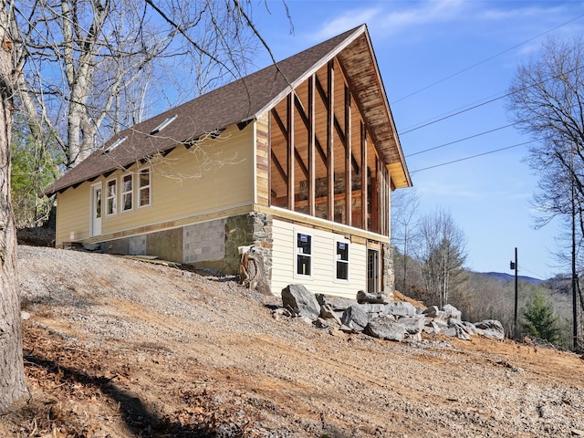 view of home's exterior with stone siding and a shingled roof