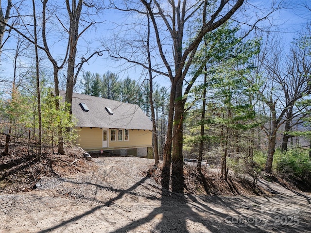 view of side of property with driveway and roof with shingles