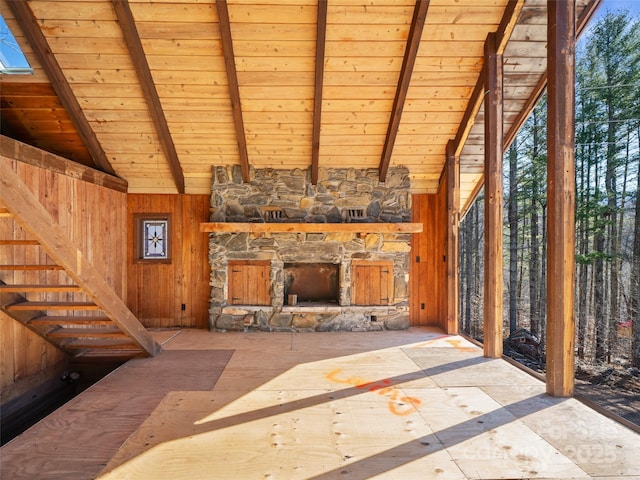 living area with wood walls, wooden ceiling, vaulted ceiling with beams, and an outdoor stone fireplace