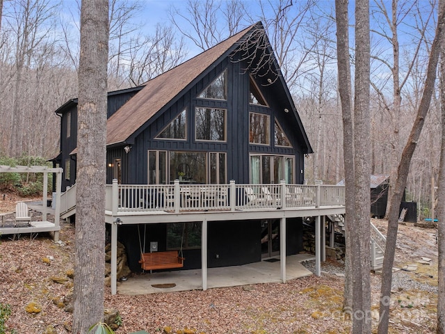 rear view of property with roof with shingles, a wooden deck, stairs, a patio area, and board and batten siding