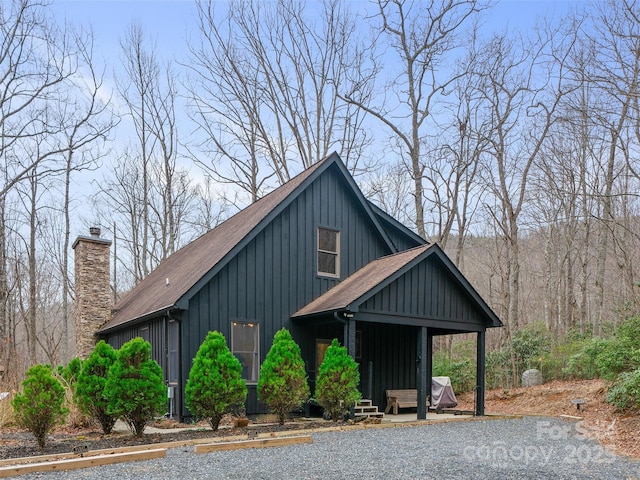 view of front of home featuring uncovered parking, roof with shingles, board and batten siding, and a chimney