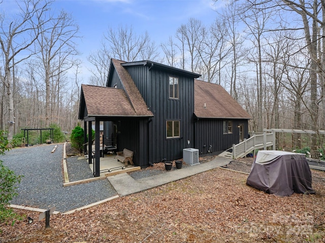 view of home's exterior with central AC unit, board and batten siding, roof with shingles, and a patio