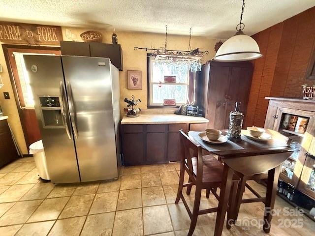 kitchen featuring light tile patterned floors, light countertops, a textured ceiling, a glass covered fireplace, and stainless steel fridge