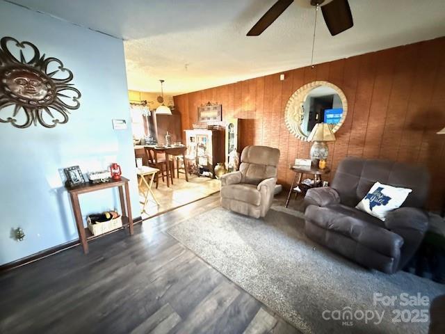 living area with wooden walls, wood finished floors, and a ceiling fan