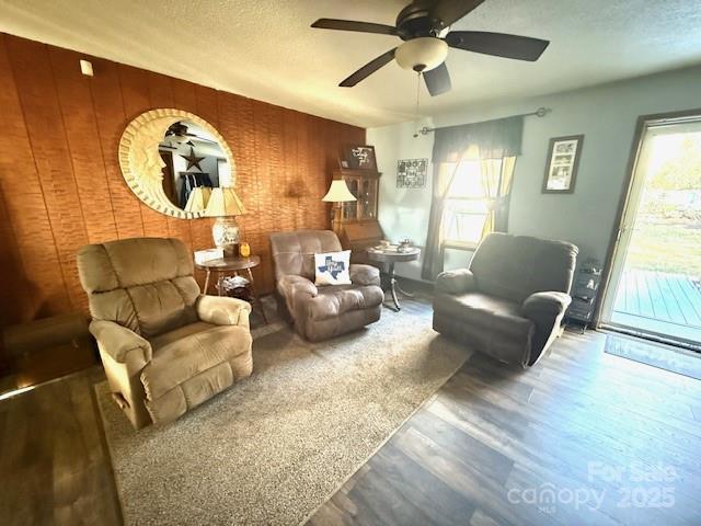 living area featuring ceiling fan, wooden walls, wood finished floors, and a textured ceiling