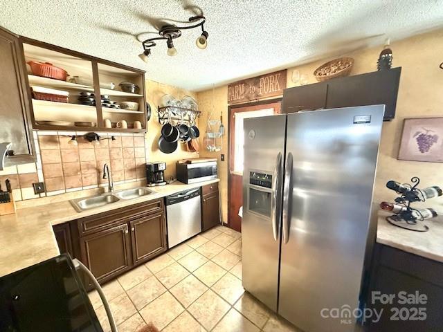 kitchen featuring a sink, a textured ceiling, stainless steel appliances, light countertops, and light tile patterned floors