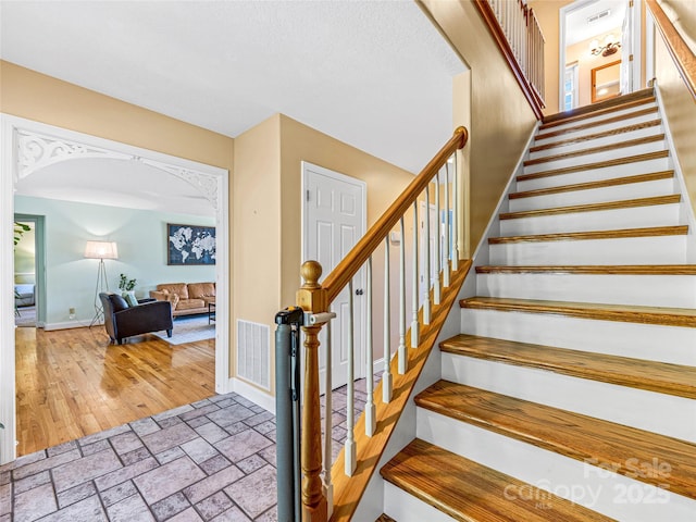 staircase with wood finished floors, baseboards, visible vents, and arched walkways