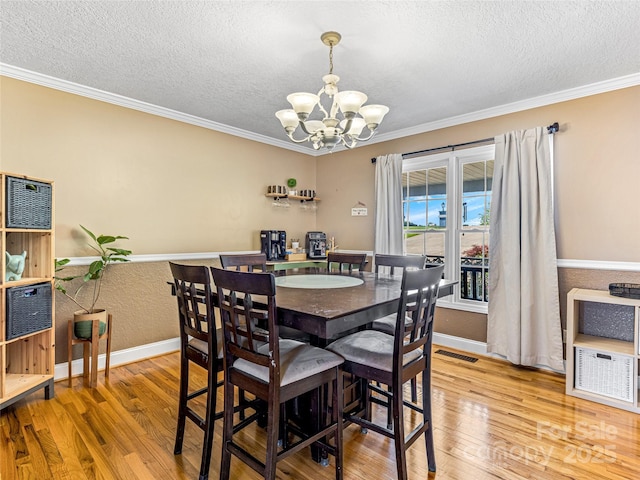 dining space with visible vents, an inviting chandelier, wood finished floors, and crown molding