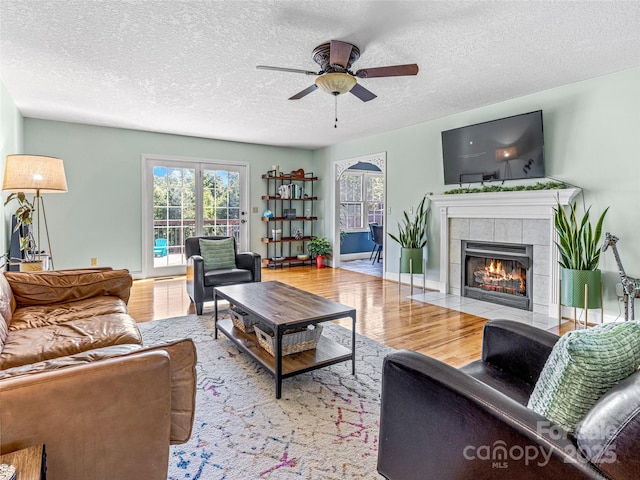 living area featuring a ceiling fan, wood finished floors, baseboards, a fireplace, and a textured ceiling