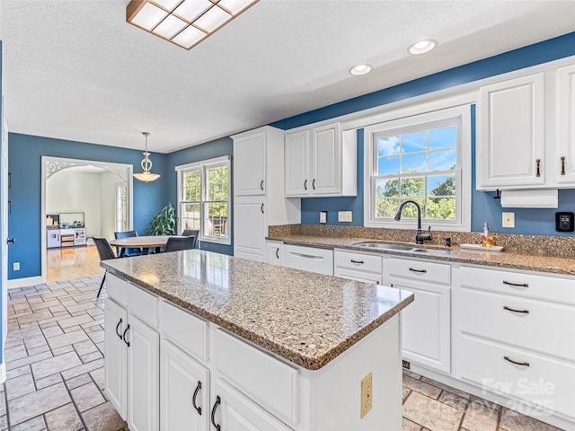 kitchen with stone tile floors, light stone countertops, a sink, white cabinets, and a center island