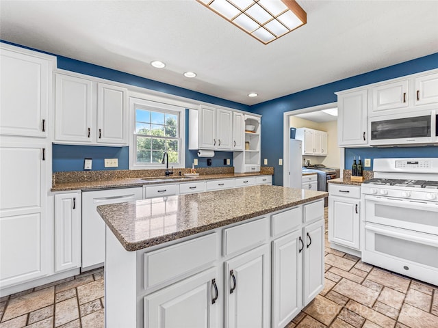 kitchen with a sink, stone tile flooring, a center island, white appliances, and white cabinets