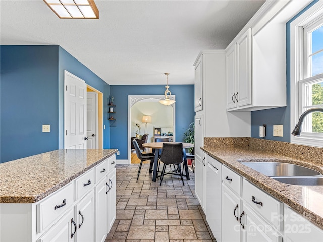 kitchen featuring pendant lighting, a sink, a textured ceiling, stone tile floors, and white cabinetry