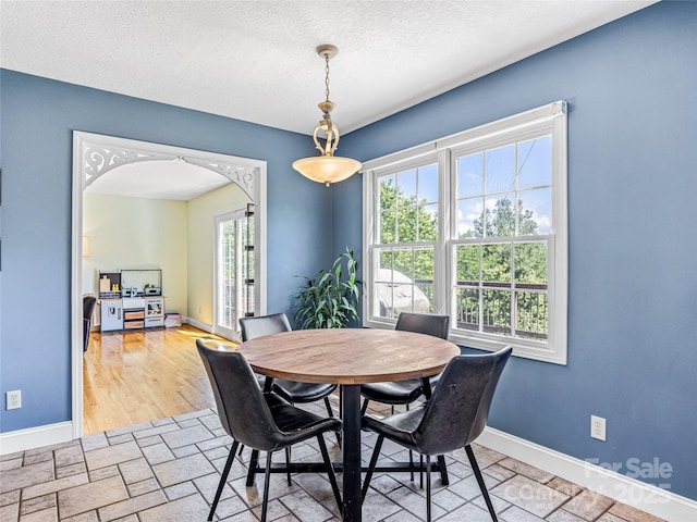 dining area featuring stone finish flooring, baseboards, arched walkways, and a textured ceiling