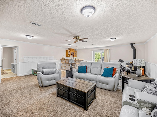 living room with visible vents, ceiling fan, light colored carpet, ornamental molding, and a textured ceiling